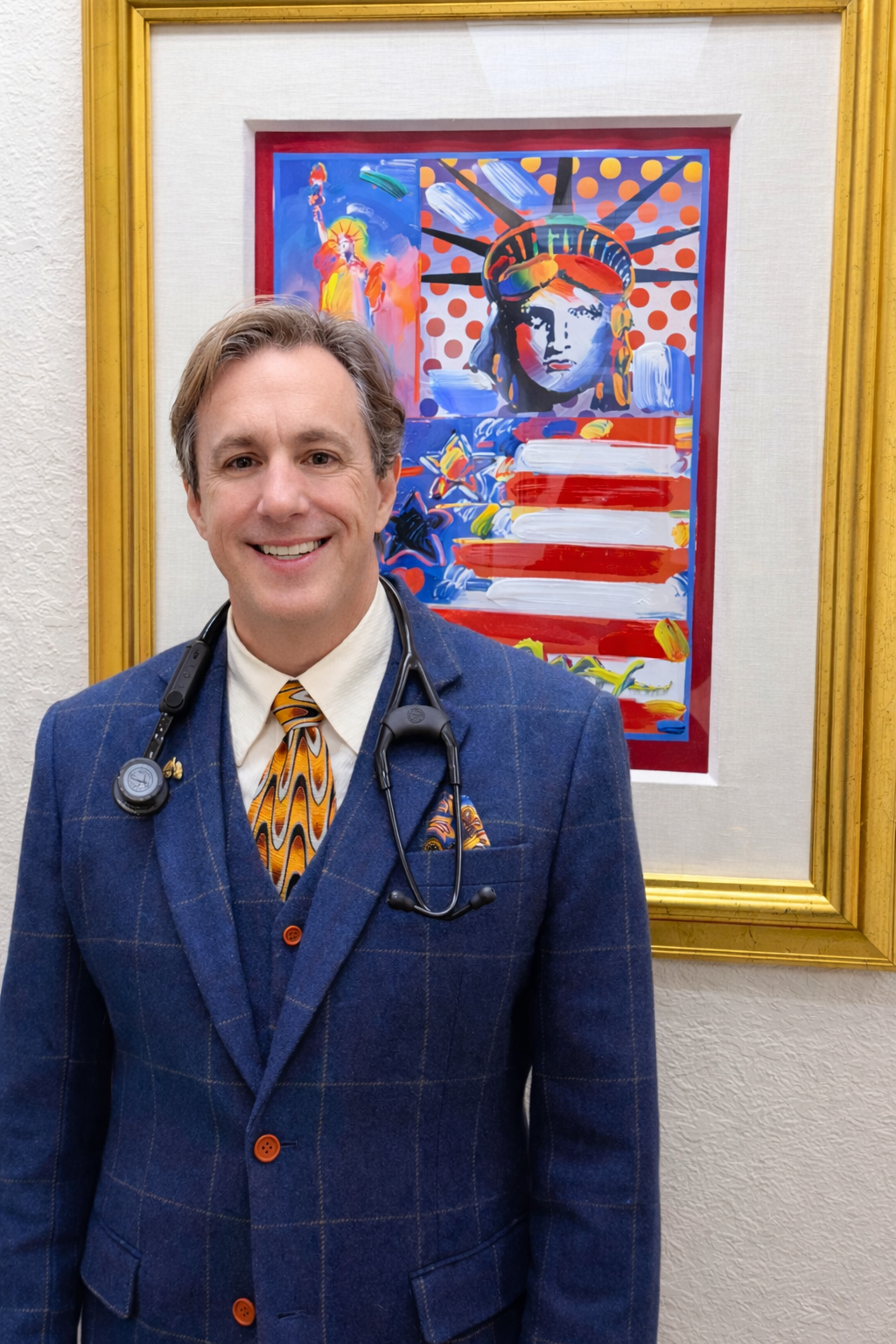 Doctor in blue suit with stethoscope stands before colorful Statue of Liberty art.