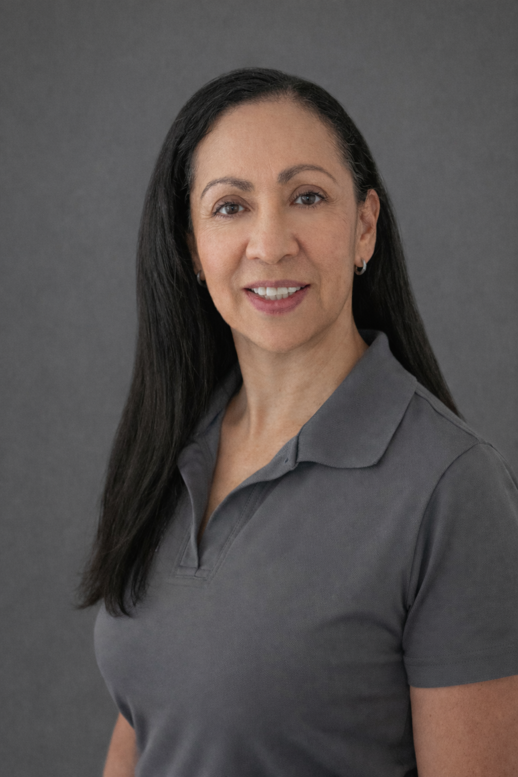 Professional woman smiling with long dark hair and gray shirt.