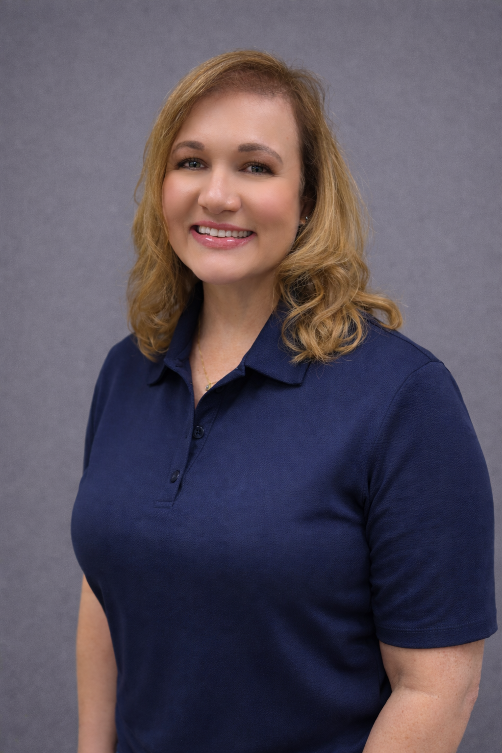 Smiling woman wearing a navy blue polo shirt against a gray background.