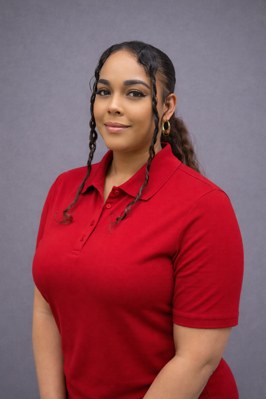 Confident woman in a red polo shirt with braided hair against a plain background.