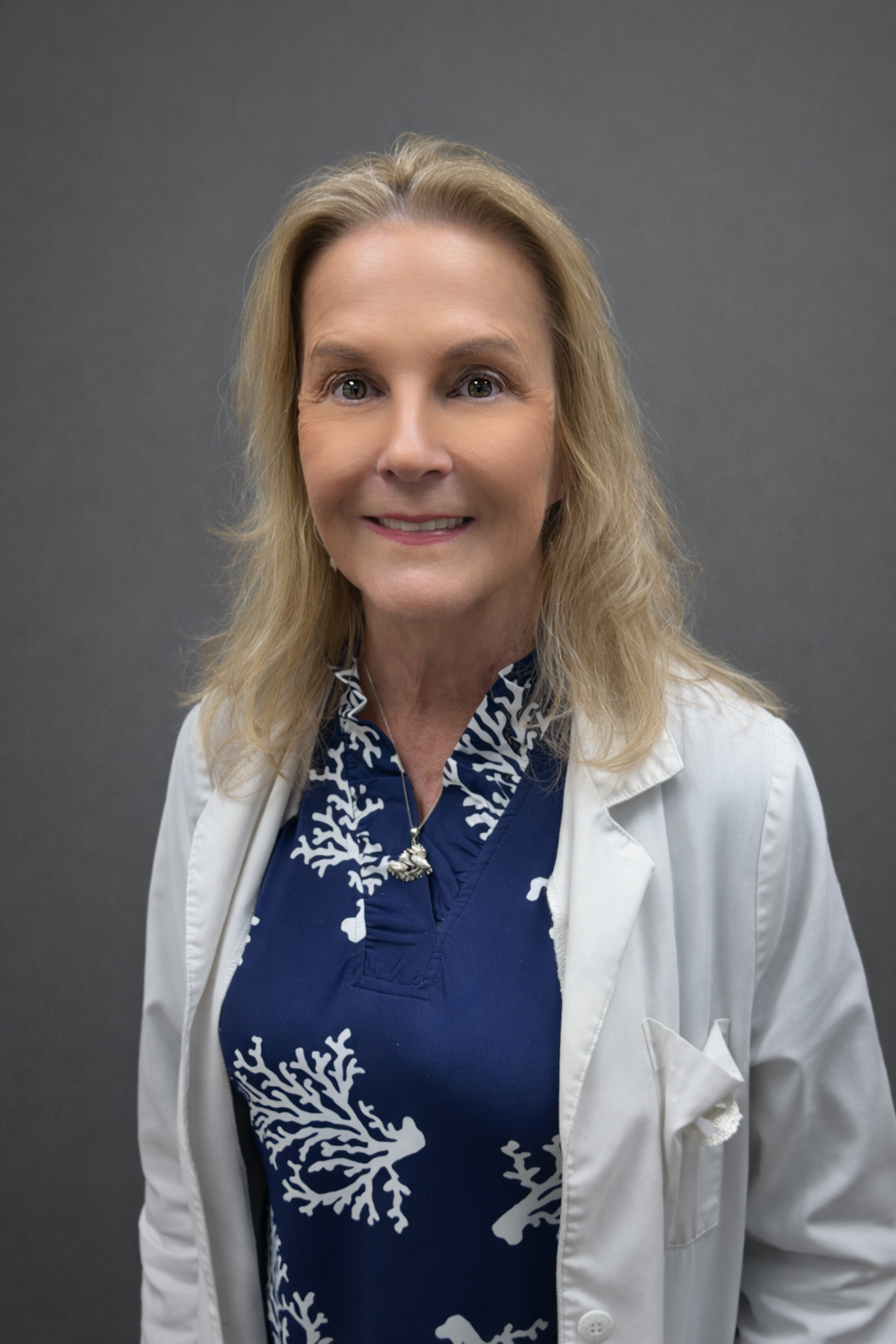 Smiling female doctor in a white coat against a gray background.