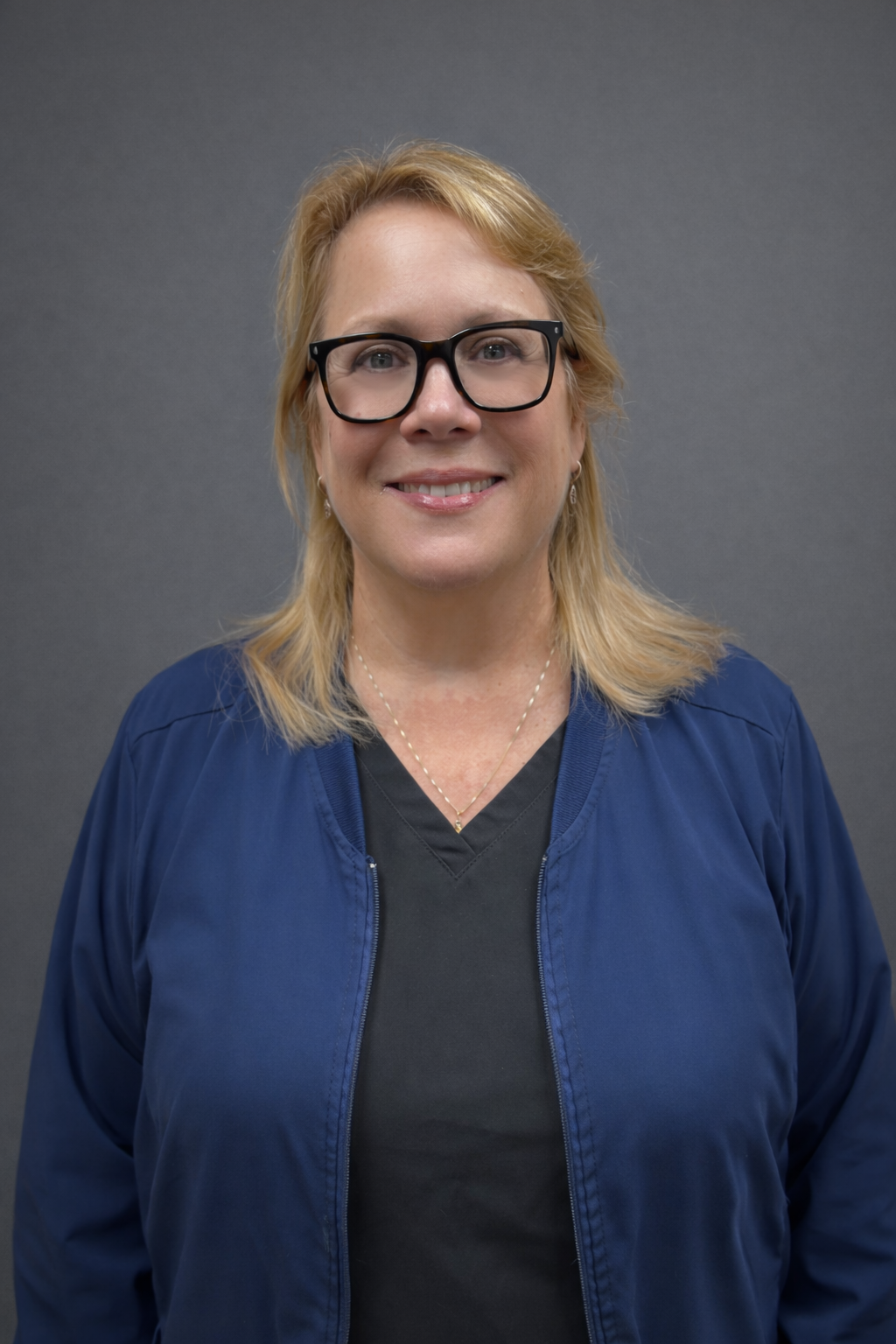 Smiling woman with glasses wearing a blue jacket and black shirt.
