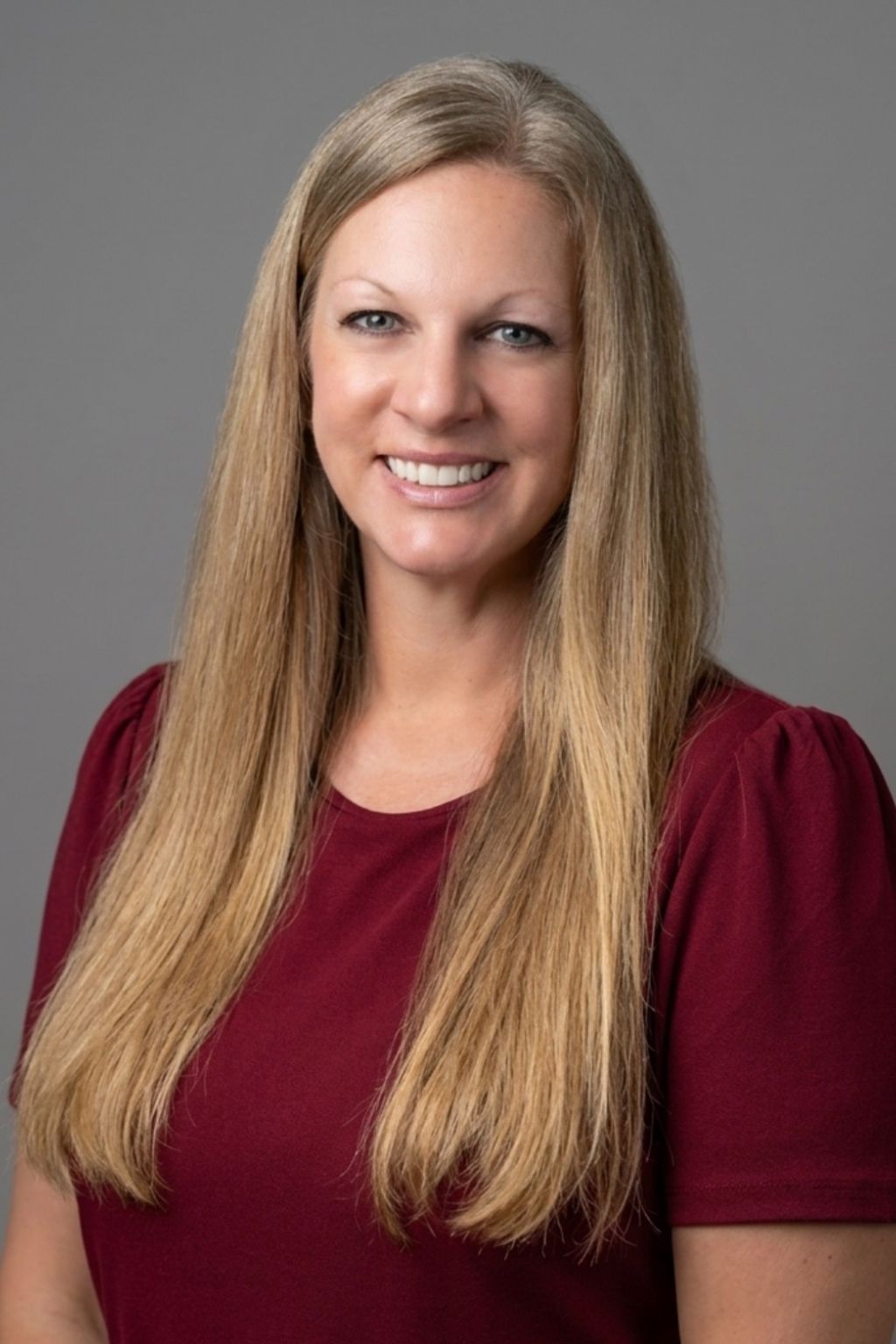 Smiling woman with long blonde hair wearing a maroon top.